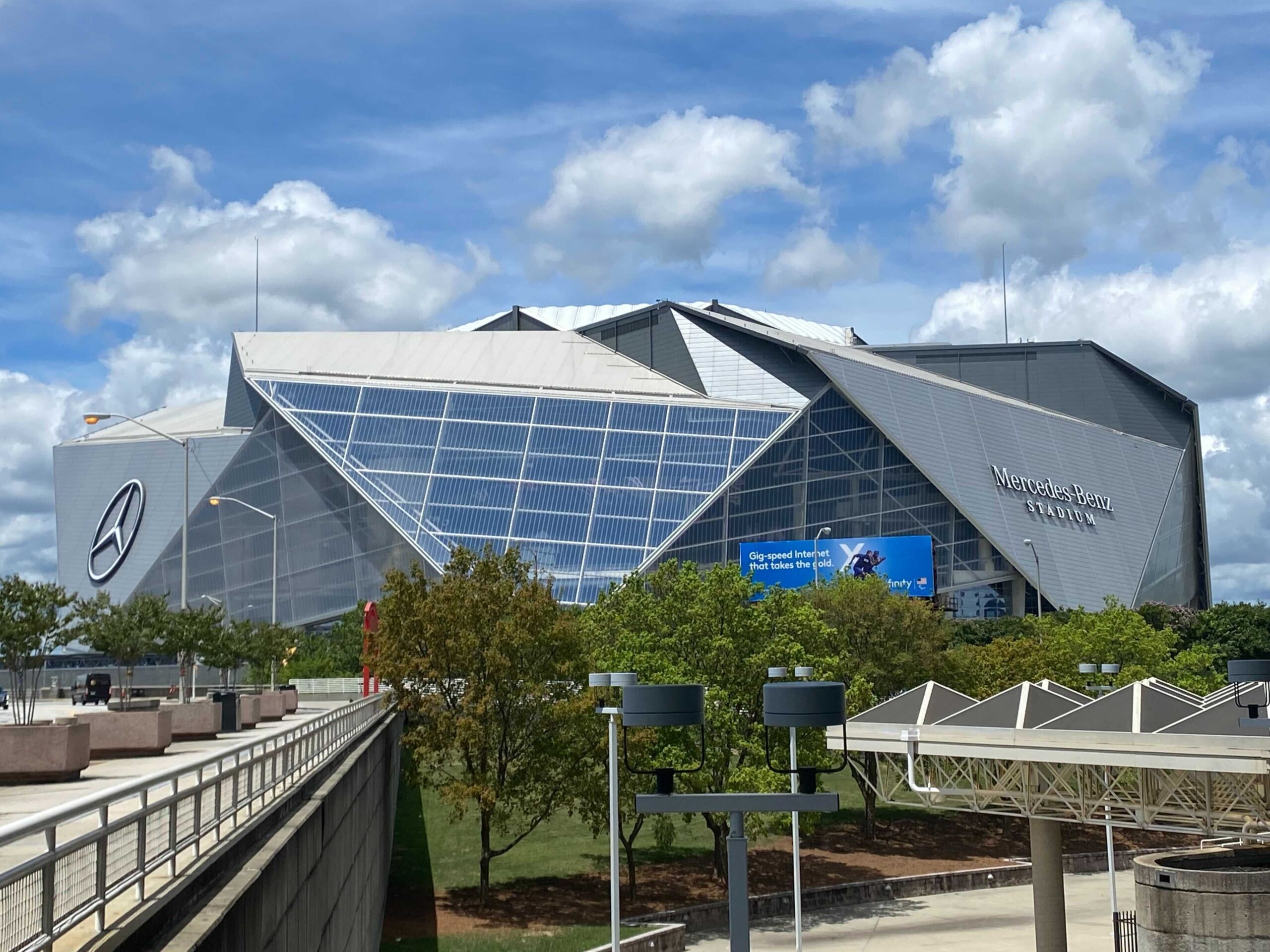 Exterior view of Mercedes-Benz Stadium with angular glass panels and a blue sky backdrop, showing the building’s distinctive modern design.