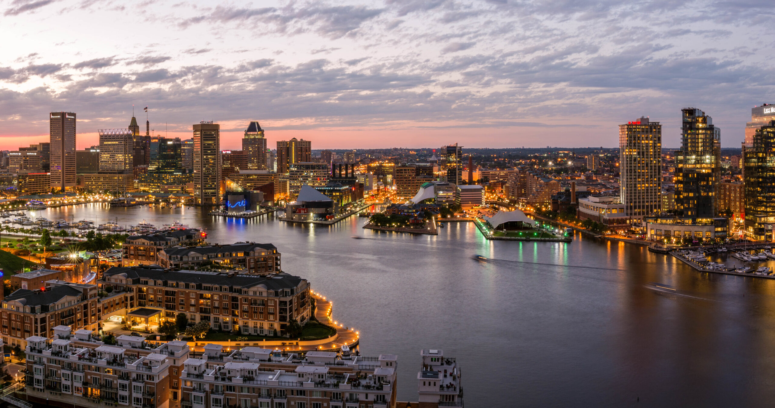 - FIND-A-STAY City skyline at dusk along a harbor with illuminated buildings and reflections in the water.