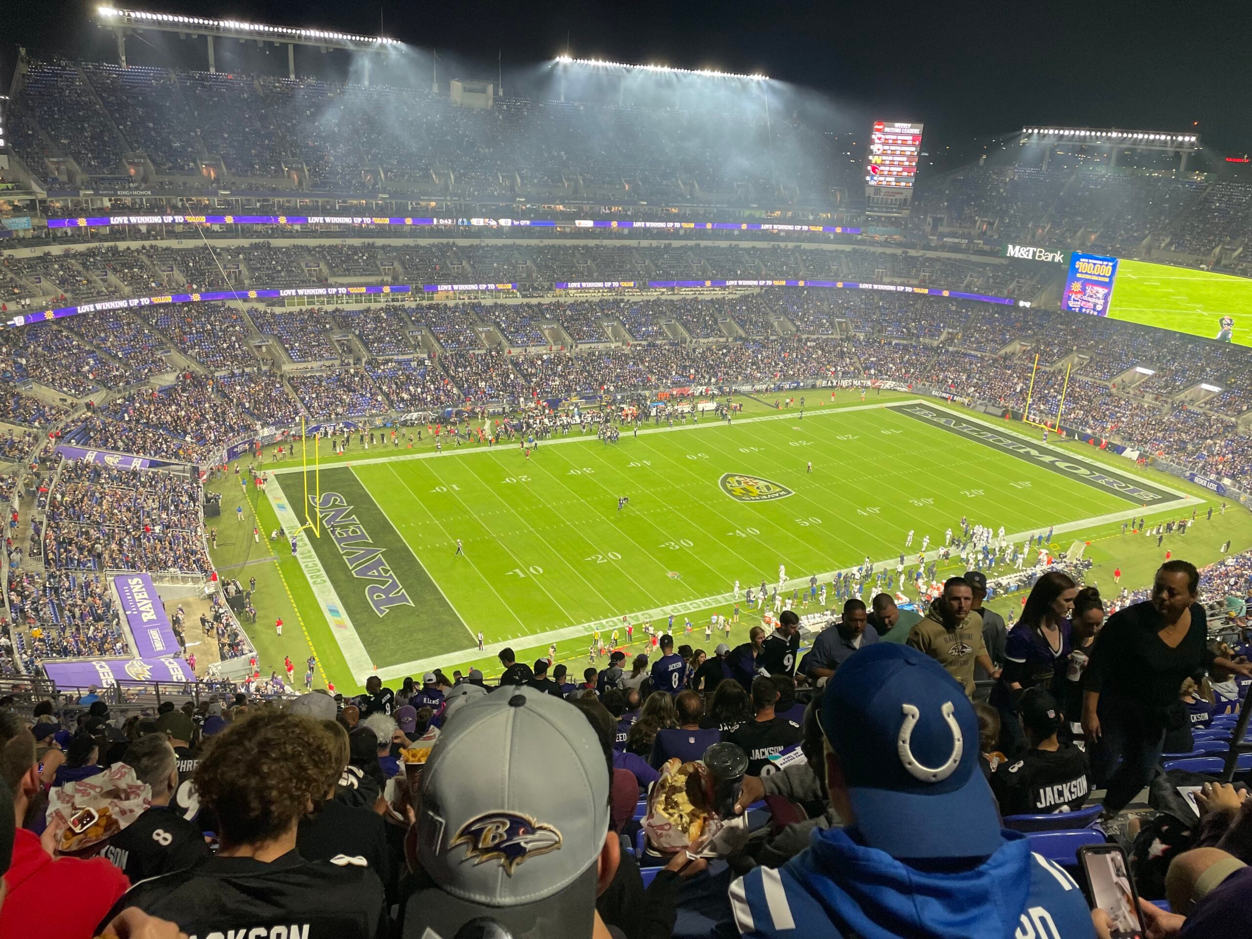 Nighttime football stadium filled with fans, bright stadium lights, and players on the field ready for action at a Ravens game.