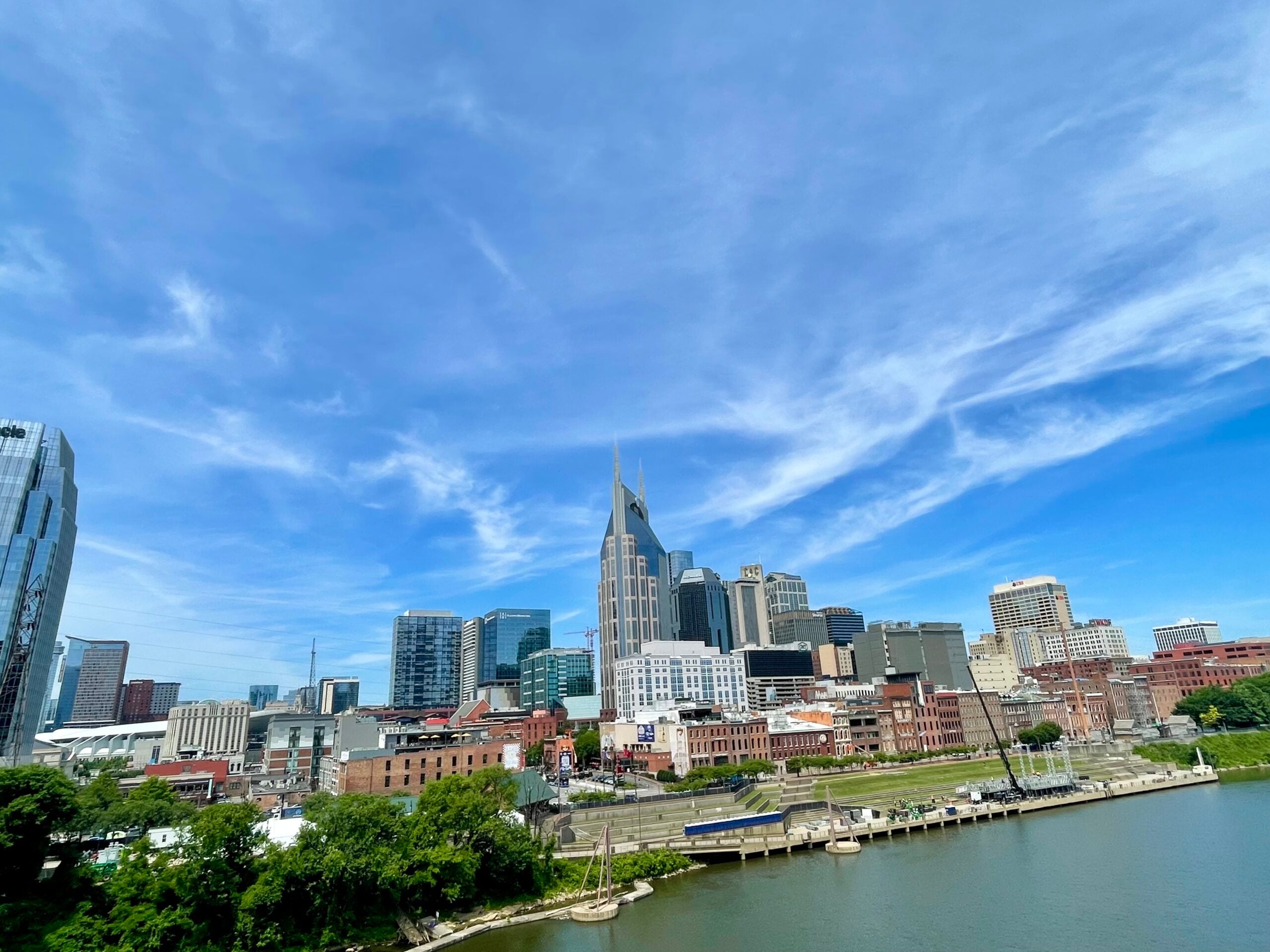 City skyline along a river under a bright blue sky with wispy clouds.