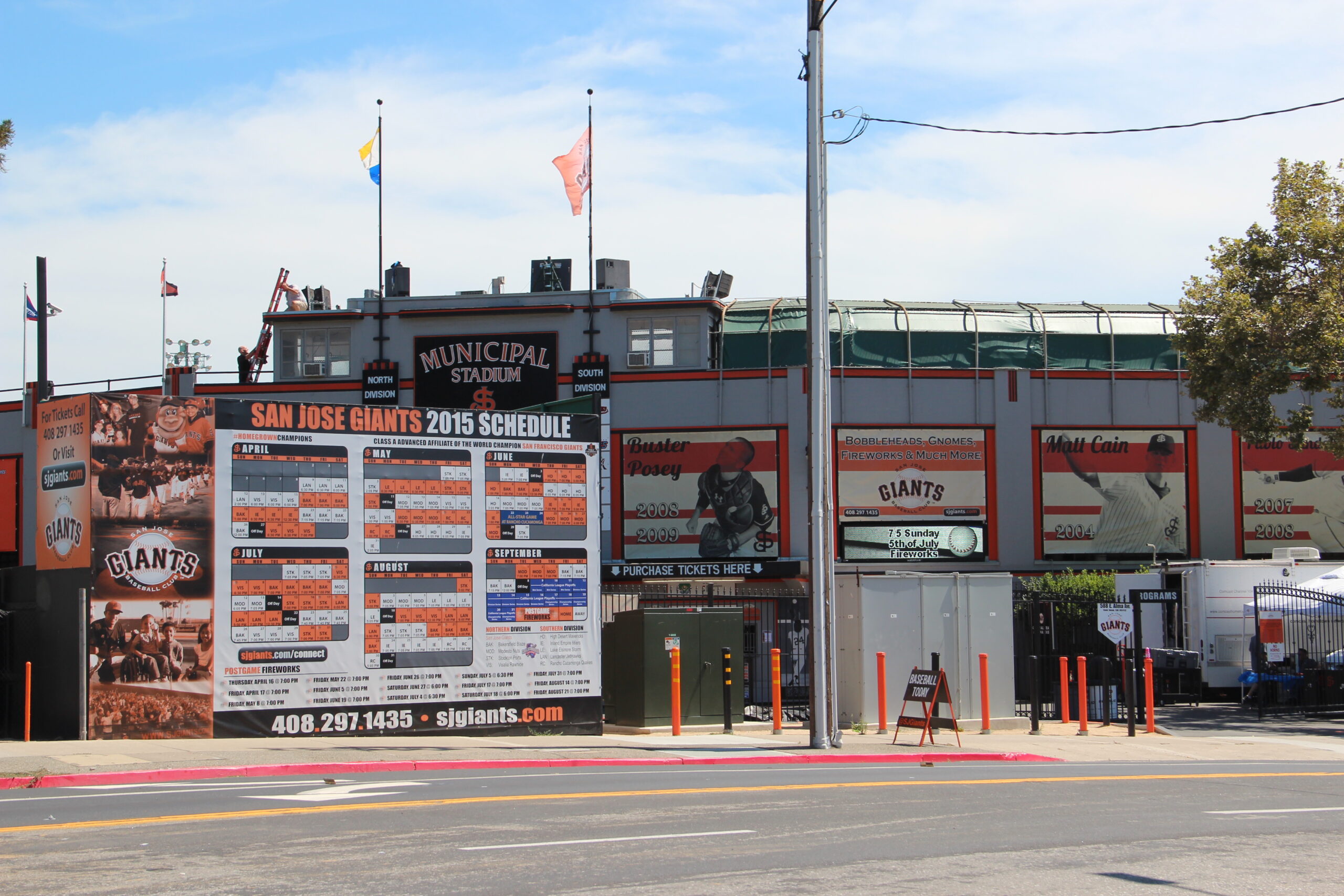 Front of a stadium with large banners and posters advertising the San Jose Giants schedule and tickets in bold red and white text.