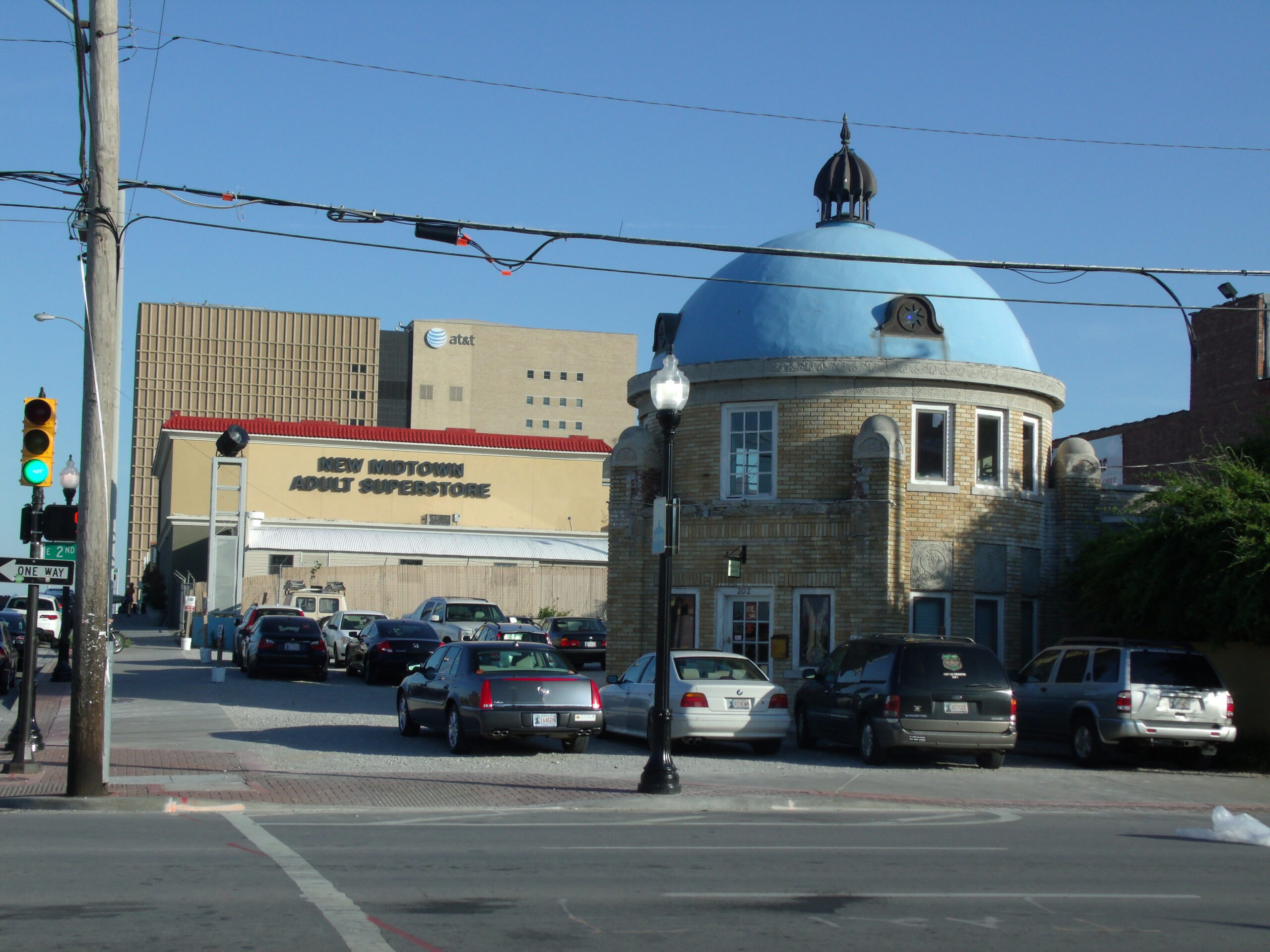 Street scene featuring a blue-domed building with a small cupola and parked cars along the curb, utility poles and overhead wires in the foreground.